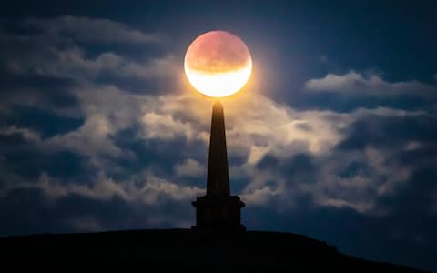 The partial lunar eclipse is visible above Stoodley Pike near Todmorden in West Yorkshire - Credit: &nbsp;Danny Lawson/&nbsp;PA