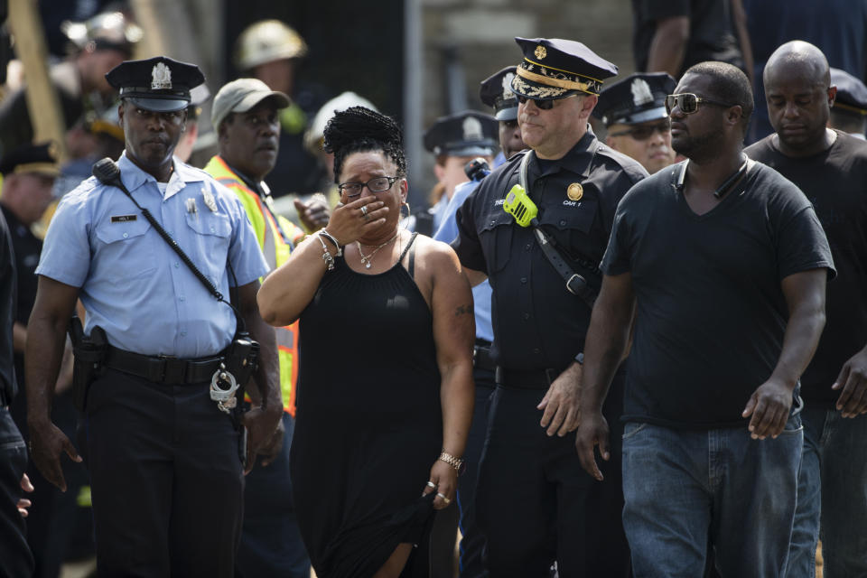 A women, accompanied by Philadelphia Fire Commissioner Adam K. Thiel, center right, reacts as rescuers work to locate and free a contractor who became trapped when a trench collapsed at a work site in a residential area of Philadelphia, Thursday, Aug. 16, 2018. (AP Photo/Matt Rourke)