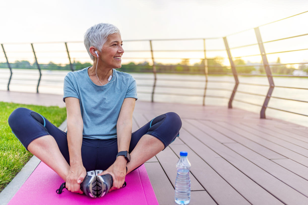 Senior woman exercising in park while listening to music. Senior woman doing her stretches outdoor. Athletic mature woman stretching after a good workout session.