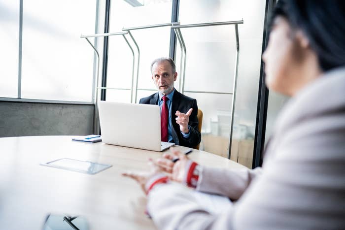 Two professionals in a meeting, one gesturing while speaking, the other listening attentively