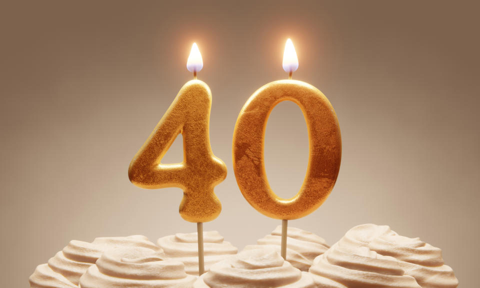 Lit golden candles shaped as number '40' on a cake topped with frosting swirls