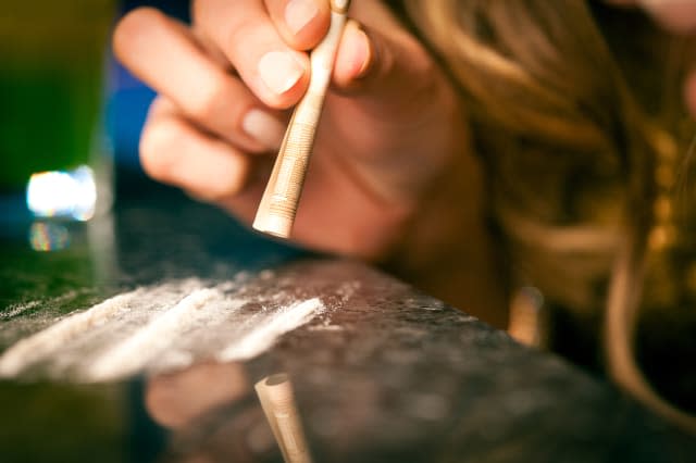 Young woman snorting cocaine with rolled up dollar