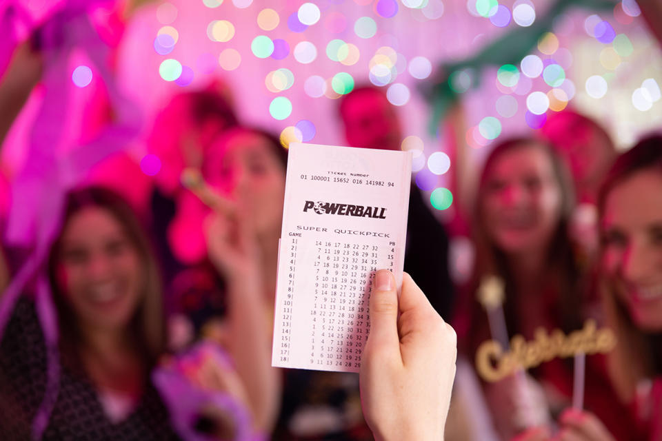 Powerball ticket held in front of celebrating crowd.