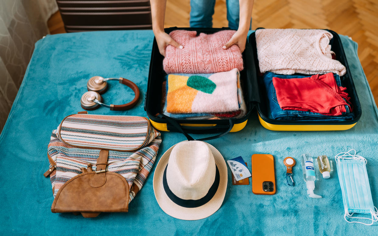 Woman packing suitcase for summer travel, including face masks and airplane travel-sized antibacterial hand gels