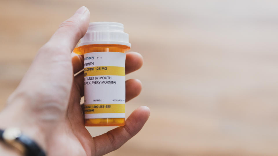 Unrecognizable man holds a pill bottle containing prescription medication.