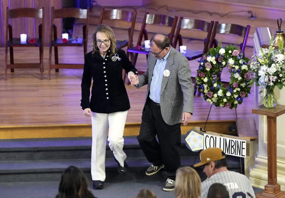 Former Arizona Rep. Gabby Giffords is helped off the stage by Tom Mauser, who is wearing his son's shoes during a vigil remembering the 25th anniversary of the Columbine High School mass shooting, Friday, April 19, 2024, in Denver. Daniel Mauser was killed during the Columbine shooting. (AP Photo/Jack Dempsey)