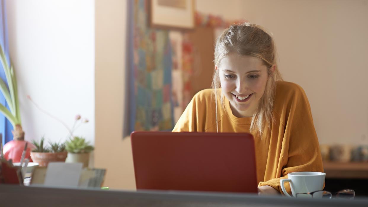  A young woman in an orange jumper using a laptop with an orange case. 