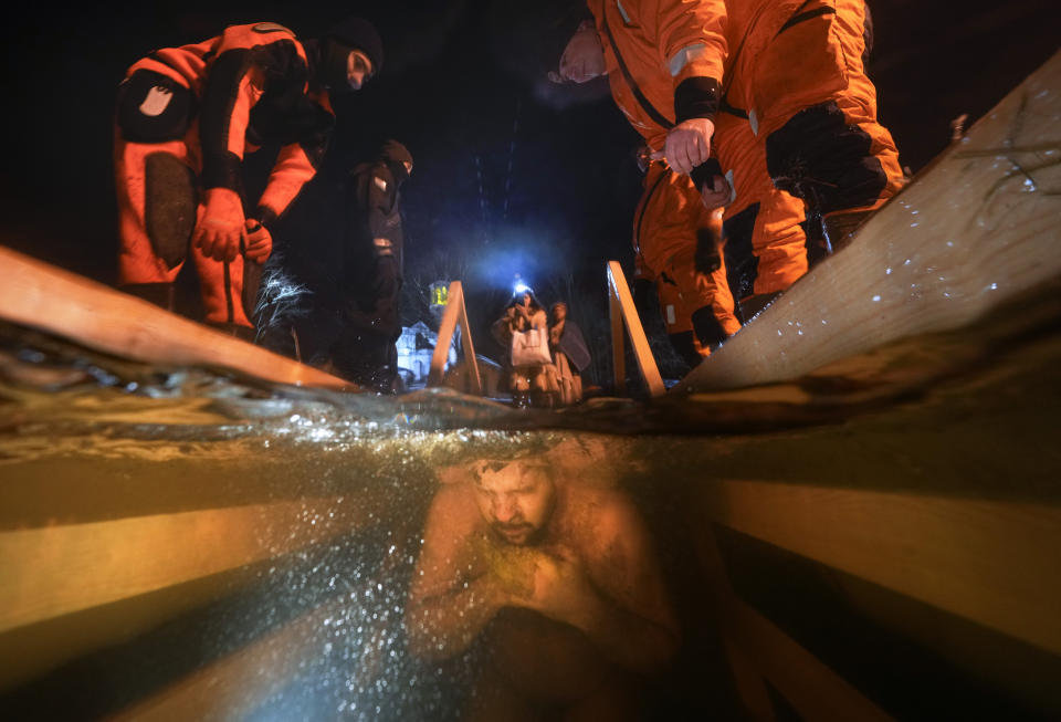 Varios rescatistas observan cómo un creyente ortodoxo ruso se sumerge en agua helada durante una celebración tradicional de la Epifanía en San Petersburgo, Rusia, el 18 de enero de 2022. (AP Foto/Dmitri Lovetsky)