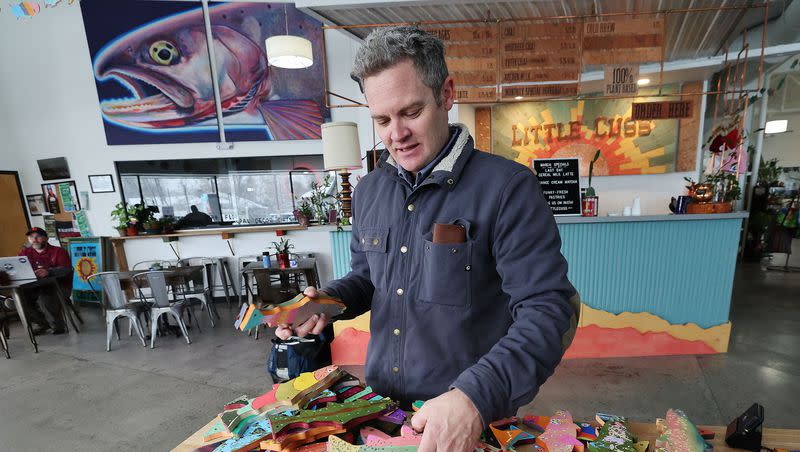 Artist Chris Peterson looks over painted fish at the Neighborhood Hive in Sugar House on Tuesday, April 4, 2023. Peterson is overseeing an art contest for the Utah Wildlife Federation.