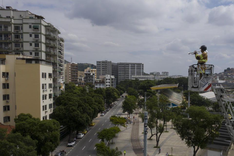 El bombero Elielson Silva toca su trompeta frente a unos edificios residenciales desde la escalera desplegada de su camión para aliviar un poco las penas de los cariocas en medio de la pandemia de coronavirus el 5 de abril del 2020 en Río de Janeiro. "Todo el mundo está sufriendo. Quiero ayudar a levantarle la moral a la gente", dice el bombero. (AP Photo/Leo Correa)