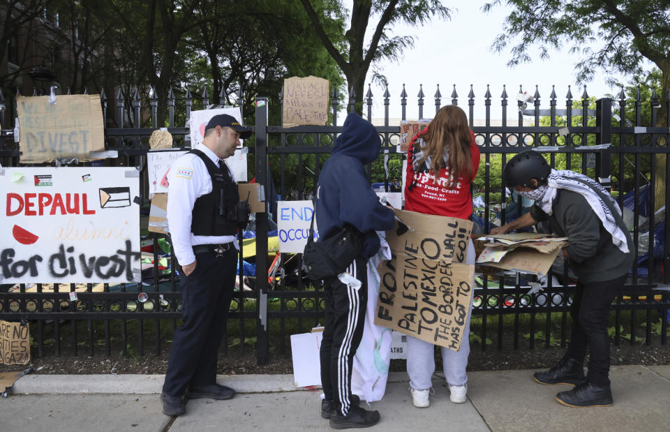 A Chicago police officer looks on as protesters remove signs from a fence around DePaul University's campus quad in Chicago, Thursday, May 16, 2024. Police dismantled a pro-Palestinian encampment at the university. The encampment was taken down in the early morning, hours after the school's president told students to leave the area or face arrest. (AP Photo/Teresa Crawford)