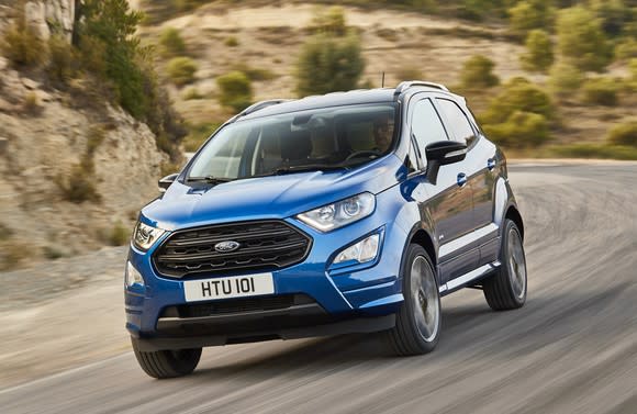 A blue 2018 Ford EcoSport, a small SUV, with UK license plate, on a country road.