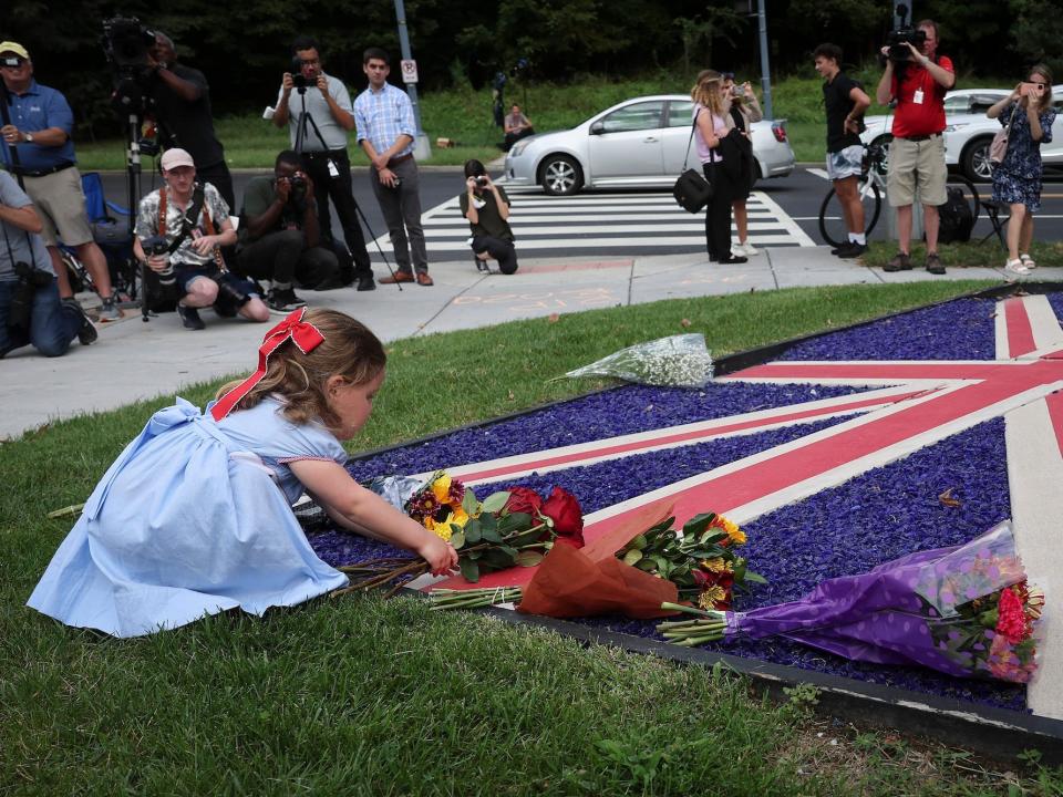 A little girl lays flowers on a British flag following Queen Elizabeth's death.