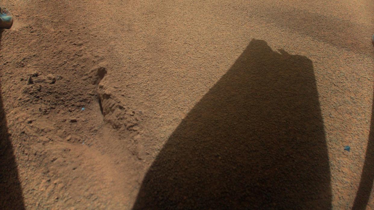  The shadow of NASA's Ingenuity Mars helicopter is cast onto the dusty Martian ground. A break at the tip of the rotor blade is clearly visible. 