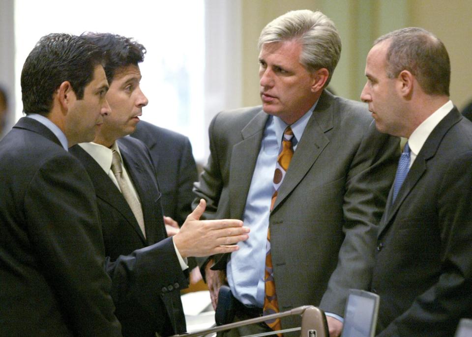 Several California Assembly members in business suits talk together.
