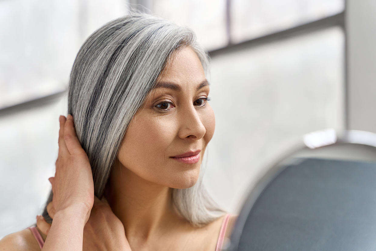 Woman touching gray hair looking at herself at mirror