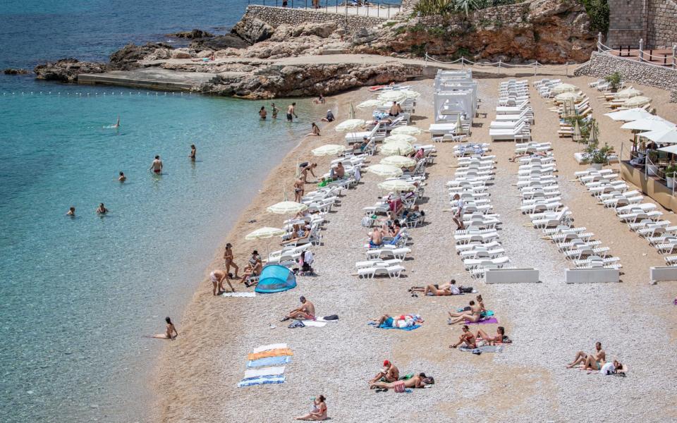 Tourists relax on the beach near the Old Town of Dubrovnik, Croatia  - Shutterstock