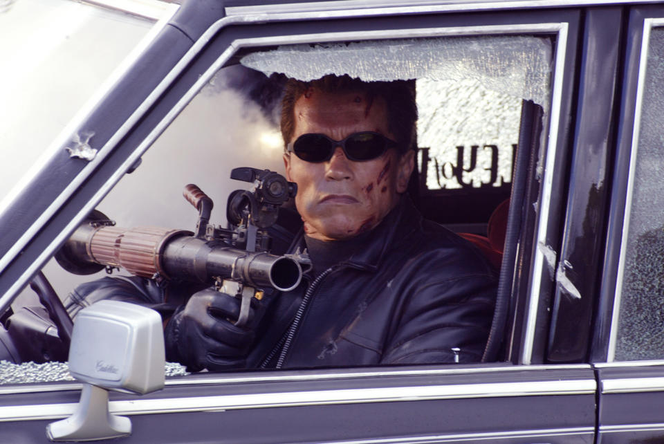 the Terminator with a gun in the driver's seat of a car with a smashed window