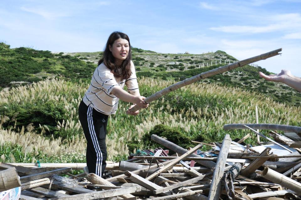 曹芷屏將一根可用的竹竿傳遞給大浦Plus團隊的夥伴，她們在馬祖東莒資源回收場的一堆廢棄物中，尋找可以用來蓋雞舍的素材。   圖：張良一/攝