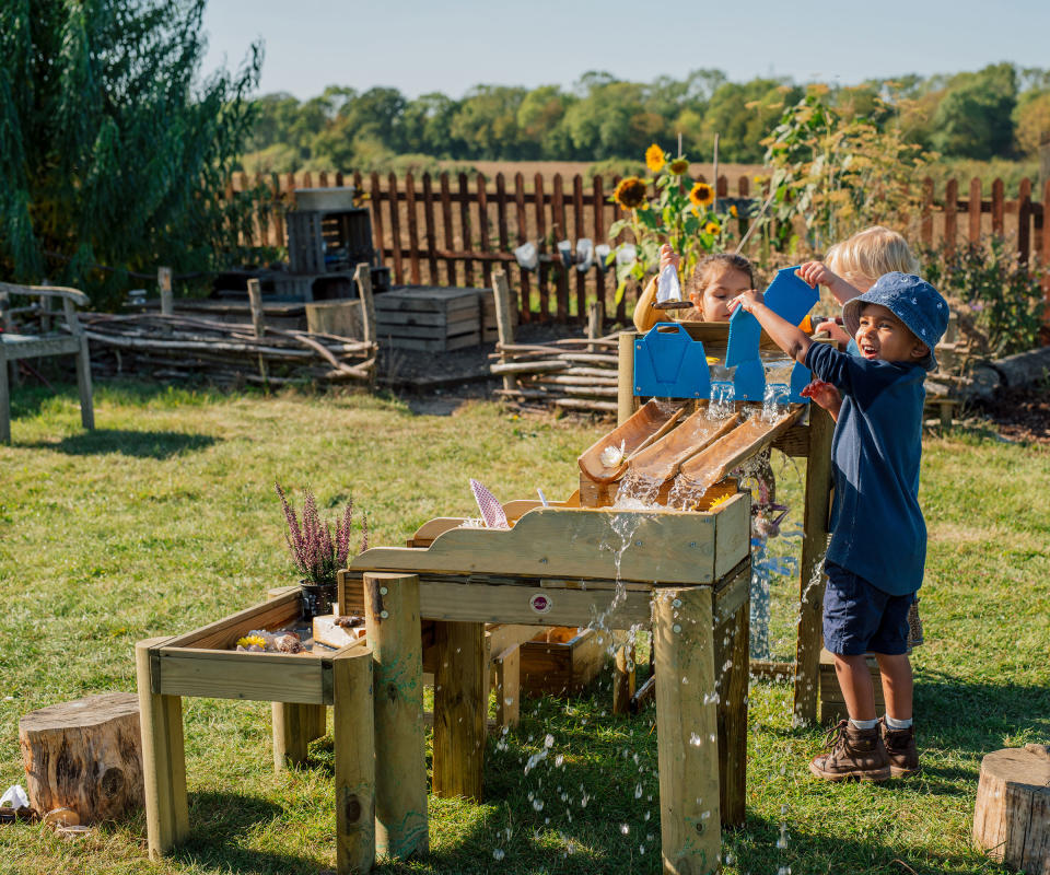 children playing at a wooden water table in a backyard