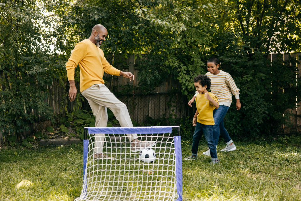 hispanic father playing soccer in the backyard with his two kids