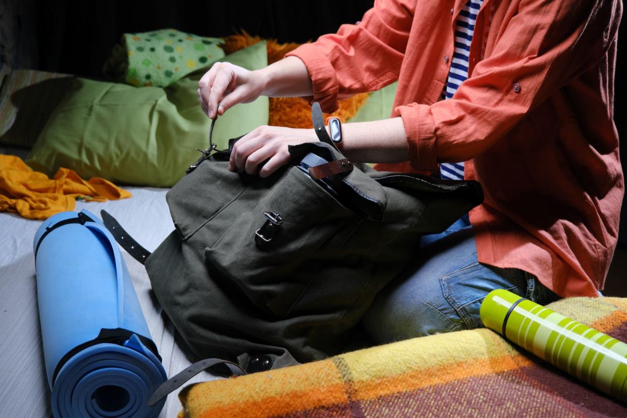 Mature person is sitting on bed and packing big rucksack for hiking