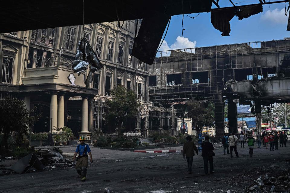 People walk under a destroyed part of the Grand Diamond City hotel-casino after a fire in Poipet on December 29, 2022. - About 10 people are dead and more than a dozen on life support after a fire at a Cambodian border casino, with photos from the scene showing people desperately huddled on ledges and perched on windowsills in a bid to escape the flames.