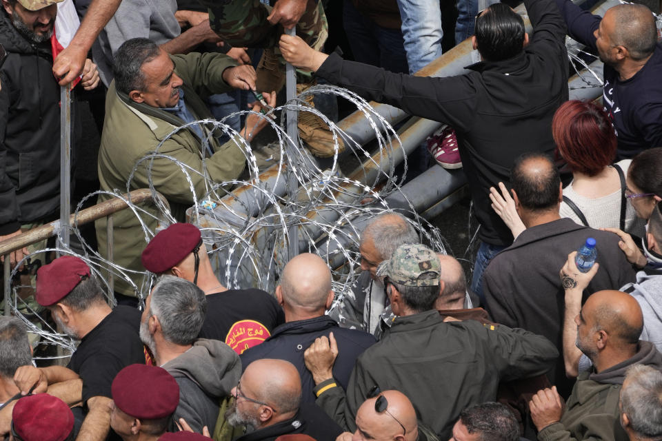 A retired army soldier, center top, cuts the wire to let other protesters to cross barriers and reach the government palace, in Beirut, Lebanon, Wednesday, March 22, 2023. Lebanese security forces fired tear gas to disperse hundreds of protesters who tried to break through the fence leading to the government headquarters in downtown Beirut Wednesday amid widespread anger over the harsh economic conditions in the country.(AP Photo/Hussein Malla)