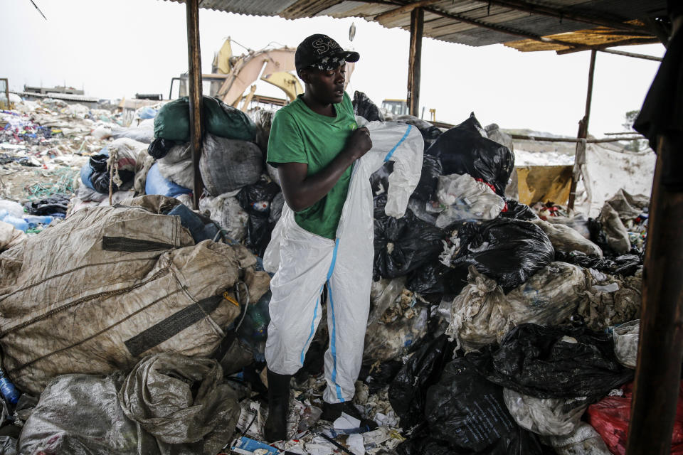 Isaac Kivai, who scavenges recyclables for a living, puts on a protective suit found in the trash at Dandora, the largest garbage dump in the Kenyan capital of Nairobi, Sunday, March 28, 2021. Trash pickers, who are not eligible for a COVID-19 vaccine shot, say the gear especially protects them from the weather during the rainy season. (AP Photo/Brian Inganga)