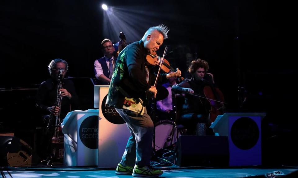 Nigel Kennedy, eyes closed and with his hair in a long crew cut, half-crouches as he plays the violin with three musicians behind him