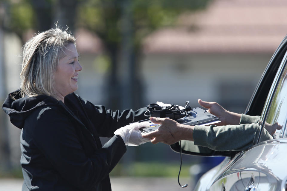 Lindsey Lilley, an employee of the Elk Grove Unified School District, hands a Chromebook to the parent of a student in the district, at Monterey Trail High School in Elk Grove, Calif., Thursday, April 2, 2020. In response to the order to close school buildings to the public due to the coronavirus, the laptops are being loaned to qualifying district families as part of the district's "distance learning" program which will be ready to go live by mid-April. (AP Photo/Rich Pedroncelli)