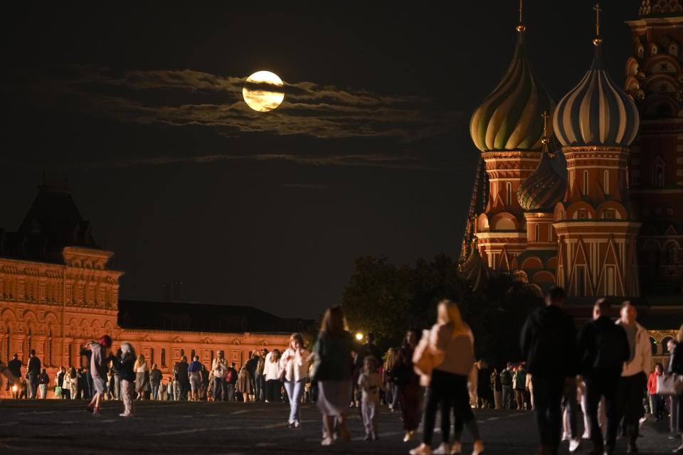 The August Super Blue Moon sets behind a historical building and the St. Basil's Cathedral, right, as people walk in Red Square in Moscow, Russia, Wednesday, Aug. 30, 2023. The cosmic curtain rises Wednesday night with the second full moon of the month, the reason it is considered blue. It is dubbed a supermoon because it is closer to Earth than usual, appearing especially big and bright. (AP Photo/Alexander Zemlianichenko)