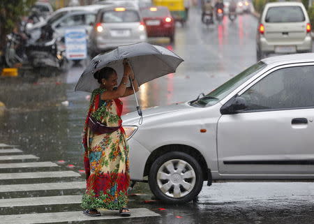 A woman tries to hold an umbrella as she walks through a busy road during a rain shower in Ahmedabad, June 24, 2015. REUTERS/Amit Dave