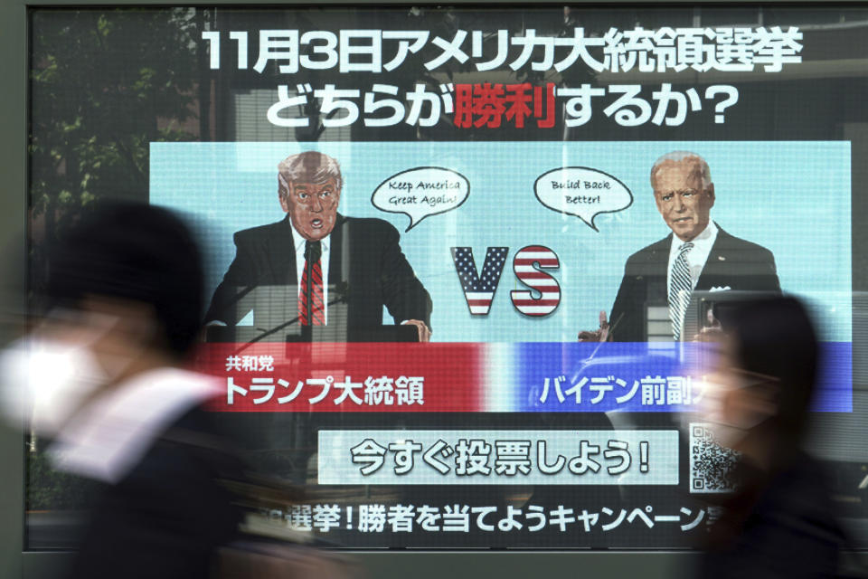 People walk past a screen showing illustrations depicting Republican President Donald Trump, left, and Democratic candidate and former Vice President Joe Biden for an online voting to predict the winner in the Nov. 3 U.S. presidential election, in Tokyo Monday, Oct. 26, 2020. The Japanese letters at top read: "Which one will win in the Nov. 3 U.S. presidential election." (AP Photo/Eugene Hoshiko)