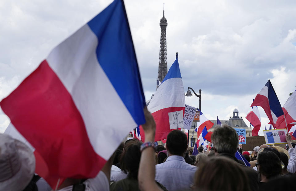 A protestor waves a French flag with a message that reads "stop the blackmail" during a demonstration in Paris, France, Saturday, July 31, 2021. Demonstrators gathered in several cities in France on Saturday to protest against the COVID-19 pass, which grants vaccinated individuals greater ease of access to venues. (AP Photo/Michel Euler)