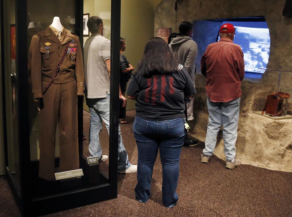 A World War II uniform with the bandolero worn by Comanche Code Talker Charles Chibbity is on display in an exhibit about the code takers at the Comanche National Museum & Cultural Center in Lawton, Okla, Thursday, Sept. 26, 2013. At right, people watch a video on the D-Day invasion at Normandy. (AP Photo/Sue Ogrocki)