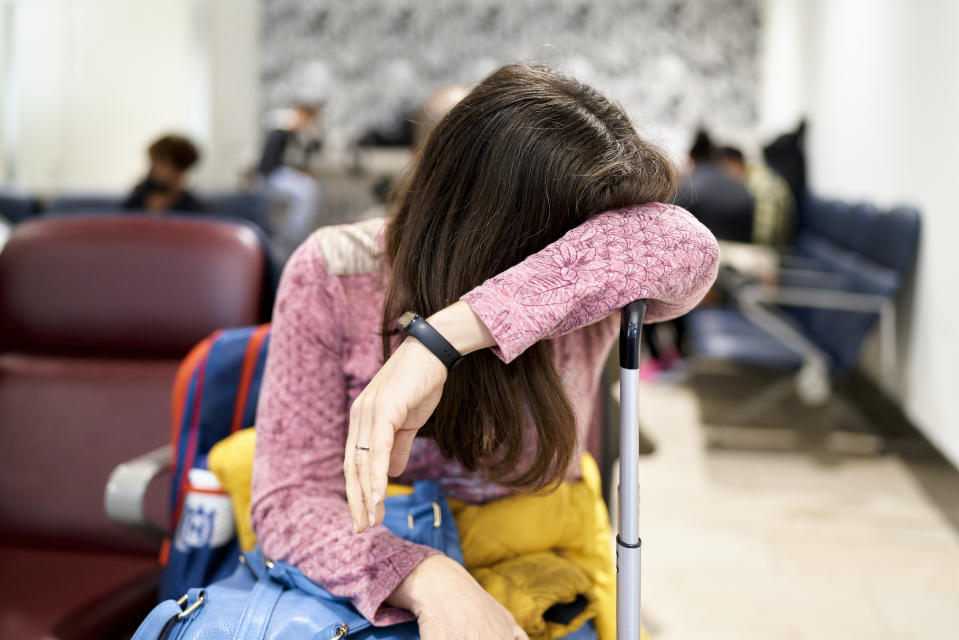 A married white woman waits in a tired position with her suitcase in the airport lounge