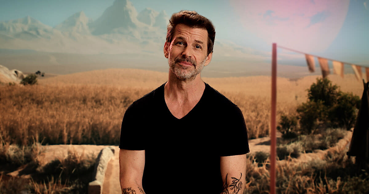  A man in a black t-shirt with a golden field and mountains in the background. 