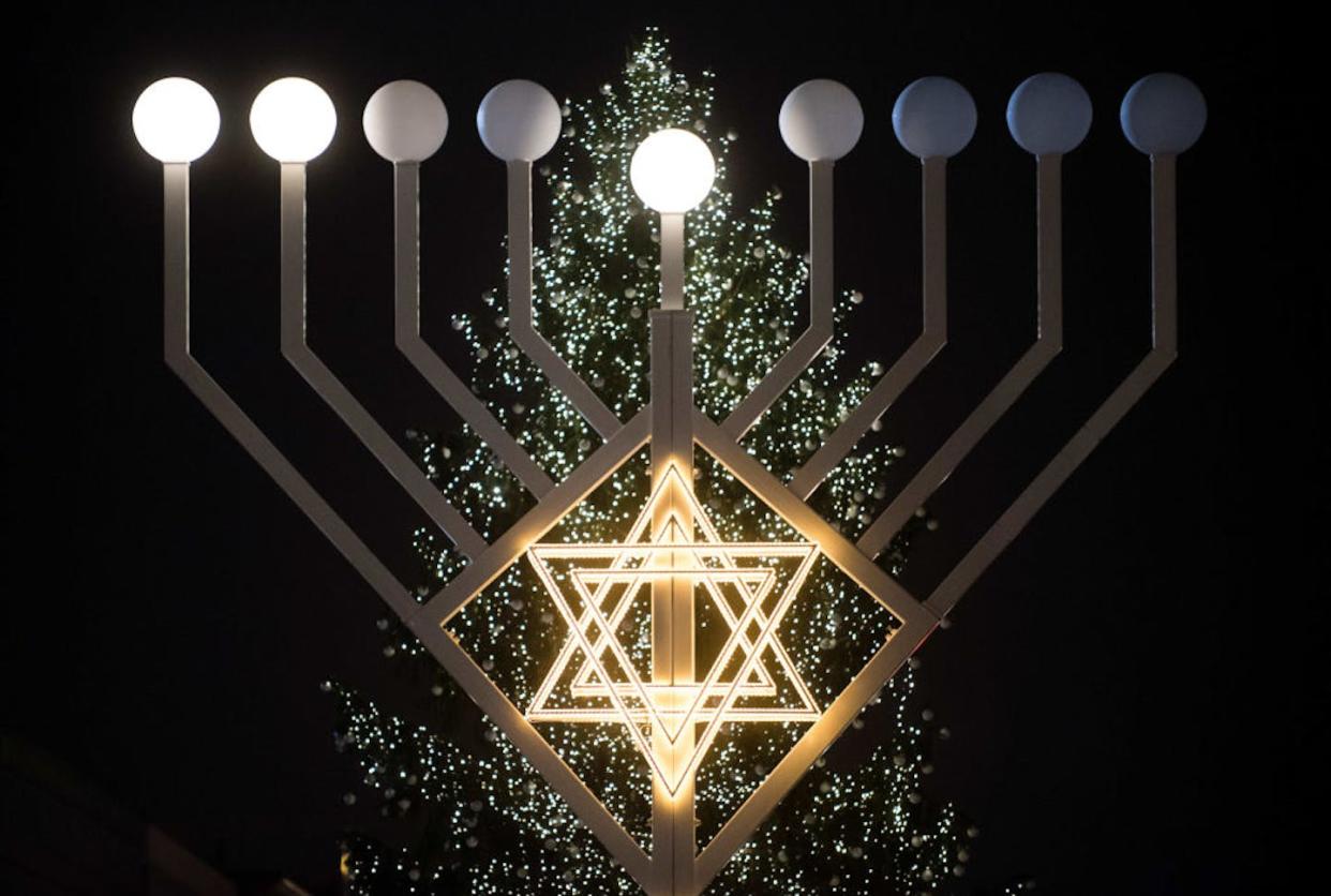 Candles on a large Hanukkah menorah shine in front of a Christmas tree at the Brandenburg Gate in Berlin, Germany, in 2015. <a href="https://www.gettyimages.com/detail/news-photo/candles-have-been-lit-on-the-10-metre-tall-hannukah-menorah-news-photo/1036787974?adppopup=true" rel="nofollow noopener" target="_blank" data-ylk="slk:Gregor Fischer/picture alliance via Getty Images;elm:context_link;itc:0;sec:content-canvas" class="link ">Gregor Fischer/picture alliance via Getty Images</a>