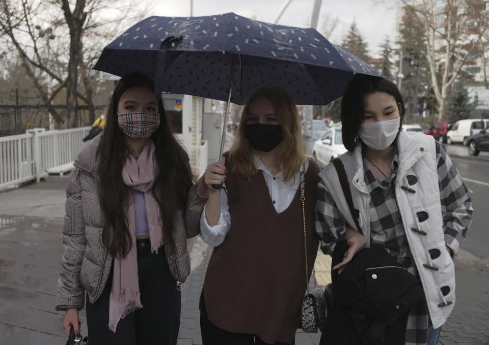 People wearing masks to help protect against the spread of coronavirus, walk in the rain in Ankara, Turkey, Monday, March 29, 2021. Turkey is reinstating weekend lockdowns in most of Turkey's provinces and will also impose restrictions over the Muslim holy month of Ramadan following a sharp increase in COVID-19 cases.(AP Photo/Burhan Ozbilici)