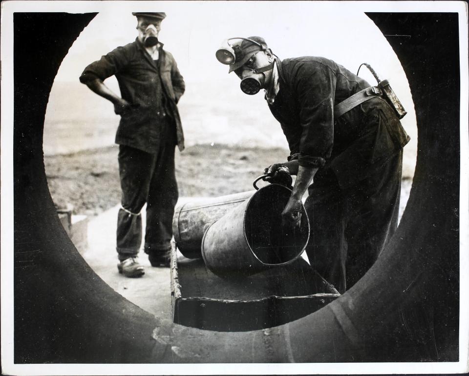 Men wearing respirators loading a four-foot wide tube with coal dust on a hilltop at Harpur Hill, Derbyshire, before detonating it in a controlled explosion for an experiment. A handful of men at the site are fighting continually against the causes of coal mine disasters. Coal dust, under certain conditions, is as dangerous as high explosive and these men are experimenting every day to find an effective method of combatting the menace. A four foot wide tube to represent a mine shaft is filled with coal dust and purposely exploded, then the burnt out dust is analysed. More deaths are caused by the gas (firedamp or methane) than the actual explosion.  (Photo by Fox Photos/Hulton Archive/Getty Images)