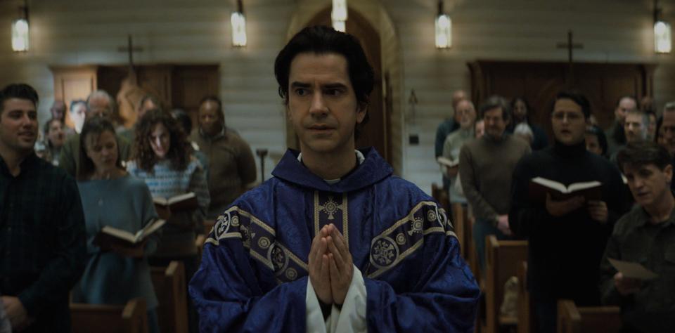 a priest stands with his hands in a prayer