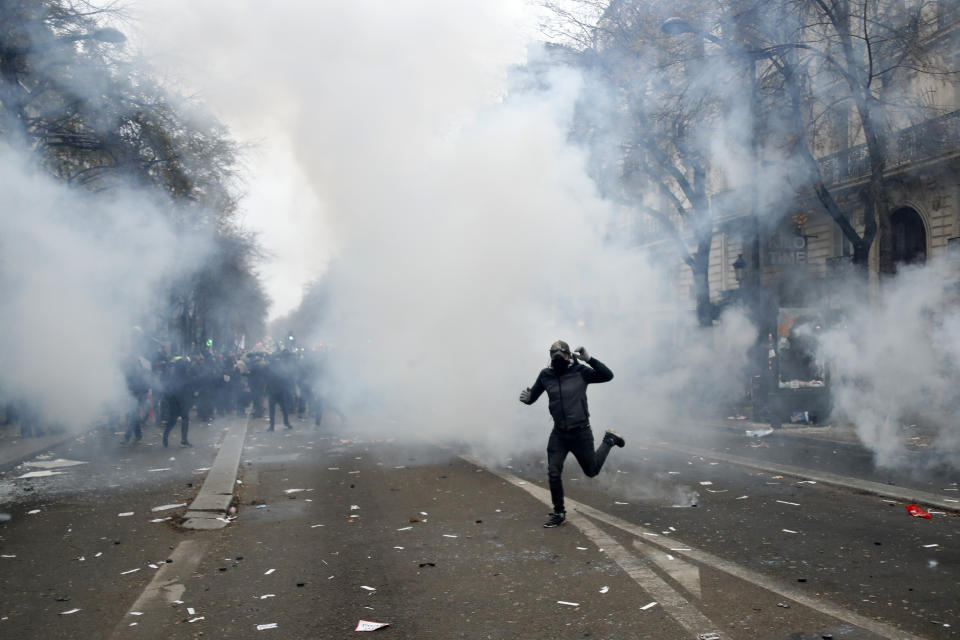 A youth runs during a demonstration in Paris, Thursday, Dec. 5, 2019. Small groups of protesters are smashing store windows, setting fires and hurling flares in eastern Paris amid mass strikes over the government's retirement reform. (AP Photo/Thibault Camus)