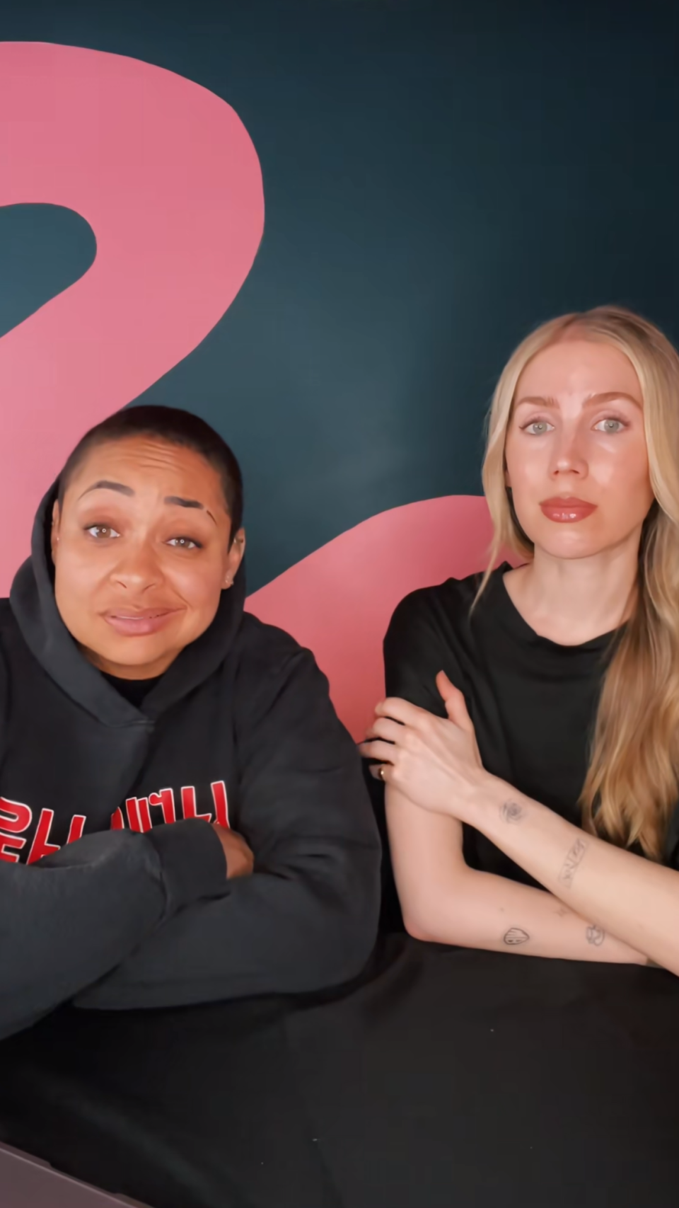 Two women posing for a selfie, one wearing a hoodie, the other with tattoos on her arm