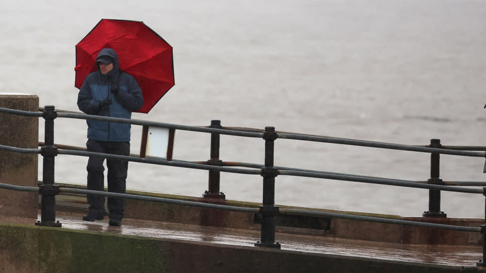 A man holding an umbrella by the coast in blustery conditions