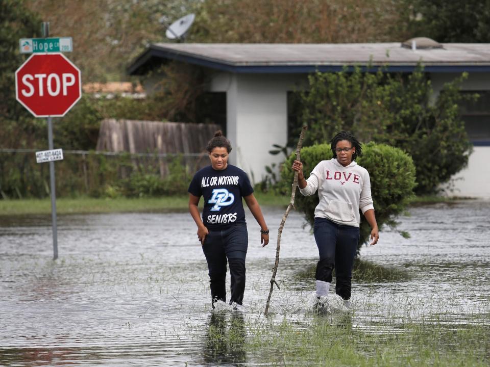 two people walk through floodwaters in residential neighborhood