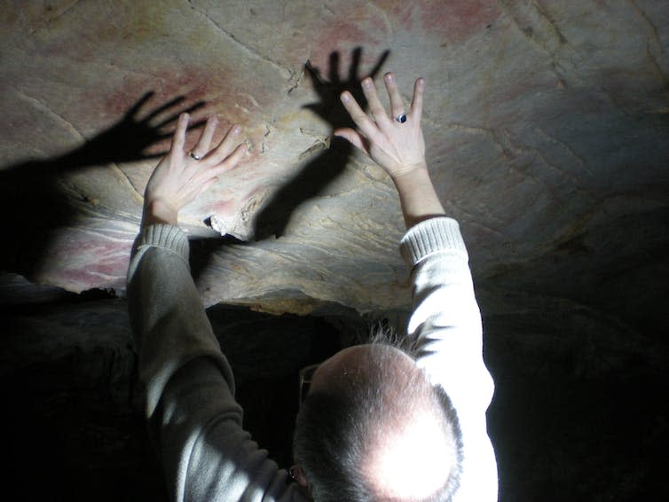 <span class="caption">In many cases hand stencils were left on parts of cave walls and ceilings that were difficult to access, such as these in El Castillo cave, with Paul Pettitt showing the position of the hands.</span> <span class="attribution"><span class="source">Paul Pettitt and cave art dating team</span>, <span class="license">Author provided</span></span>