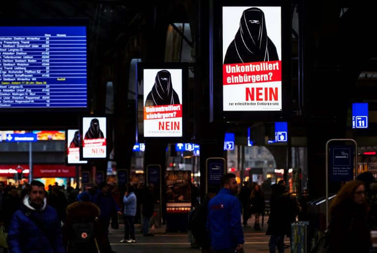 People walk past electoral posters by the Committee Against Facilitated Naturalization/Citizenship reading "Uncontrolled Naturalisation? No" with the illustration of a woman wearing a niqab, in a train station in Zurich, on February 7, 2017