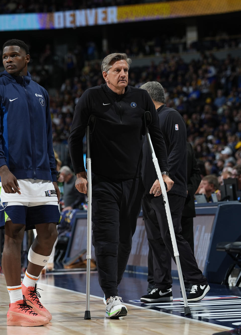 Minnesota Timberwolves head coach Chris Finch, right, walks with crutches as guard Anthony Edwards, left, looks on in the second half of Game 1 of an NBA basketball second-round playoff series against the Denver Nuggets, Saturday, May 4, 2024, in Denver. (AP Photo/David Zalubowski)