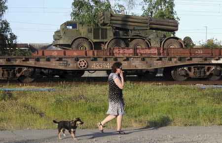 A multiple launch rocket system is seen on a freight train platform as a woman and a dog pass by in the Russian southern town of Matveev Kurgan, near the Russian-Ukrainian border in Rostov region, Russia, May 23, 2015. REUTERS/Stringer